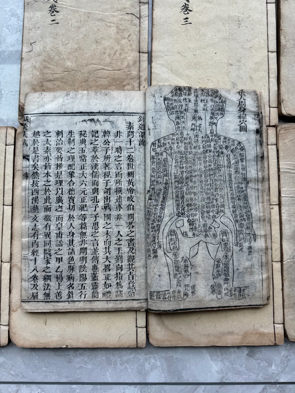 图片展示的是《针灸大成》中的人体经络图。图中经络线条清晰，标注了多个穴位名称，如足三里、内关等。图下方有大量文字说明，详细介绍了经络的走向、分布及功能等。图片位于介绍《针灸大成》的上下文之后，直观呈现了书中经络知识的平面形式，与上下文提到的纸上的经络是直线、知识是静止的观点相呼应，体现了知识与身体的立体关系。