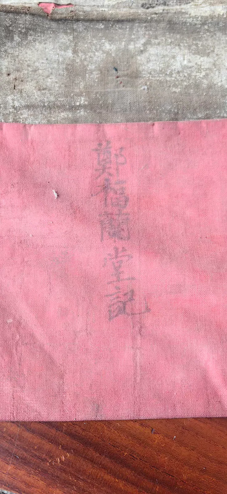 图片展示的是“郑福兰堂记”针灸包的特写。包首为粉红色布料，上面用黑色线绣有“郑福兰堂记”五个字，字体为竖排。包的边缘有磨损痕迹，底部放置在木质桌面上。图片与上下文紧密相关，上下文提到“郑福兰堂记”四个字绣在包首，既是品牌标记，也像一句承诺，这些针要进入诊疗，让书上知识在手上活过来，此图直观呈现了这一品牌标记。