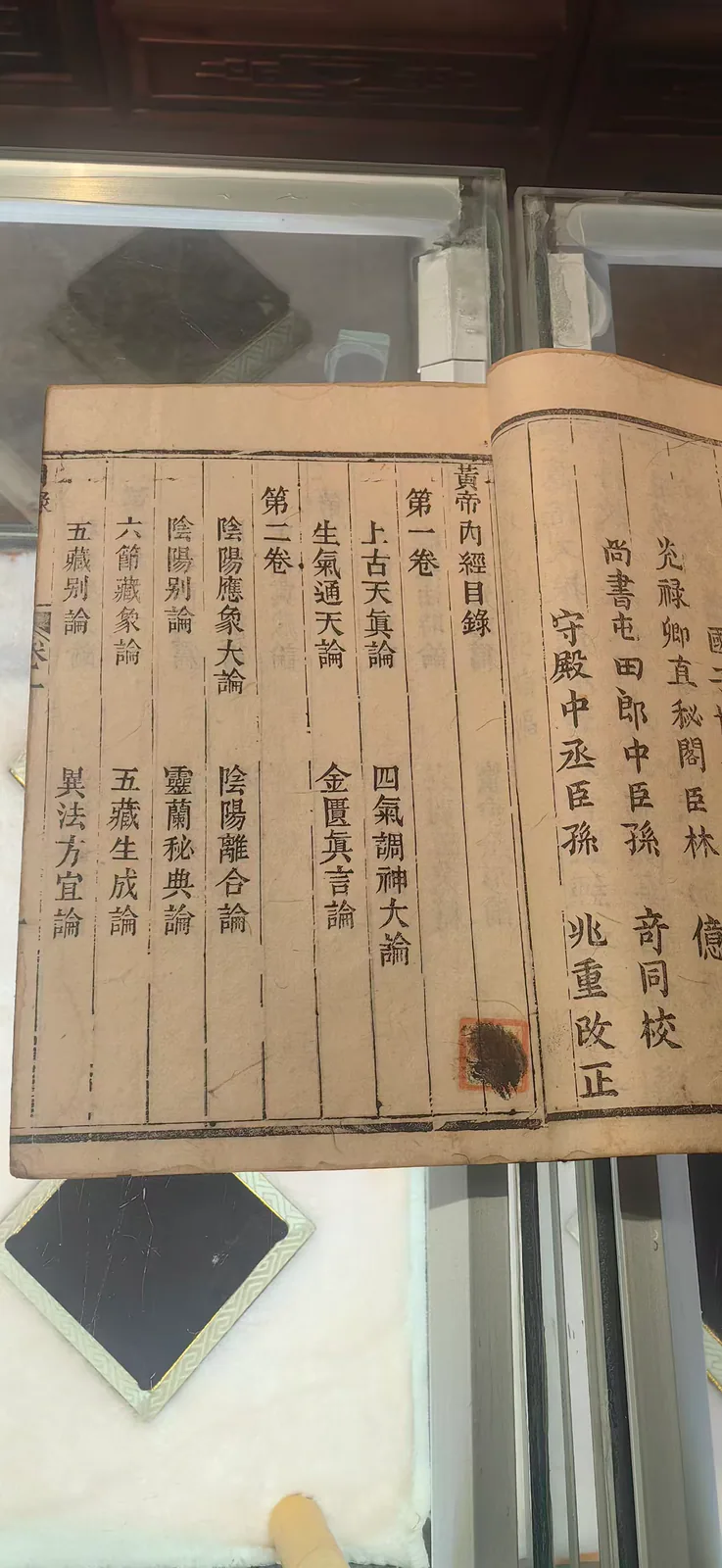 图片展示的是郑福兰堂珍藏版《黄帝内经》的书影细节。书页上清晰地印有繁体字目录，分为第一卷和第二卷，第一卷包括上古天真论、四气调神大论等，第二卷有阴阳应象大论、灵兰秘典论等内容。书页边缘有明显的折痕，左侧书页上还贴有黑色标签。此图片与上下文紧密相关，直观呈现了书中目录，呼应了上文提到的《黄帝内经》是中医学理论基石这一内容。