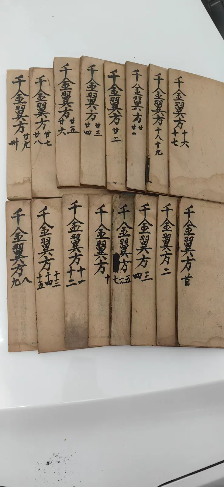 这是郑福兰堂所藏《千金翼方》的内页书影，图中整齐排列着多册旧纸质古籍，古籍册脊处用黑色毛笔手写标注书名及卷次、册次，如“千金翼方首”“千金翼方二”“千金翼方九”“千金翼方廿一”等，字迹为繁体书写，古籍纸张呈陈旧的黄褐色，保留着旧书古朴的质感，这些古籍是该堂将《千金翼方》列为镇堂典籍的实物佐证，对应文档中关于这部典籍作为镇堂瑰宝的相关内容。