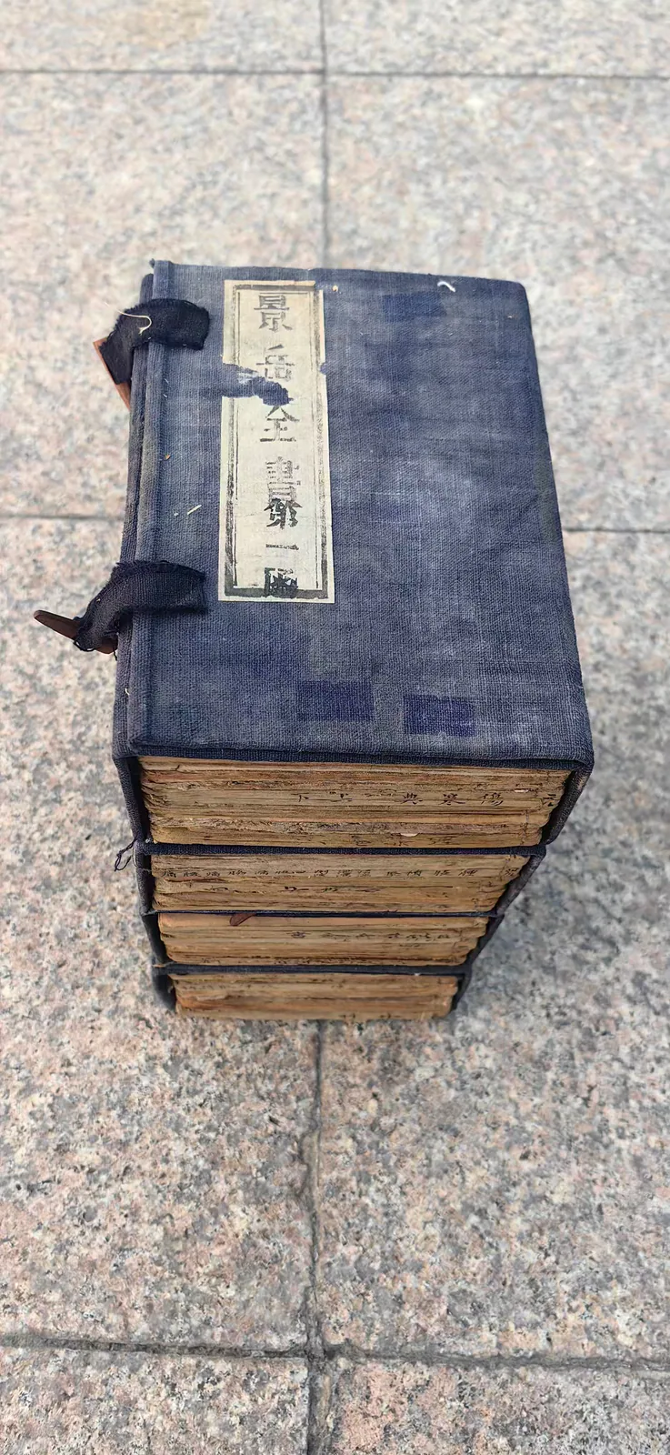 图片展示了郑福兰堂珍藏版《景岳全书》（多册叠放）。书册为深蓝色布面装订，封面上有“景岳全书第一册”字样，书签清晰可见。书册整齐叠放于地面上，地面上铺有灰色石砖。该图片与上下文紧密相关，直观呈现了郑福兰堂所珍藏的《景岳全书》实物，体现了其在临床指导上的重要性，与文档中对《景岳全书》为中医入门与进阶必读经典，郑福兰堂将其视为“实战指南”的介绍相呼应。