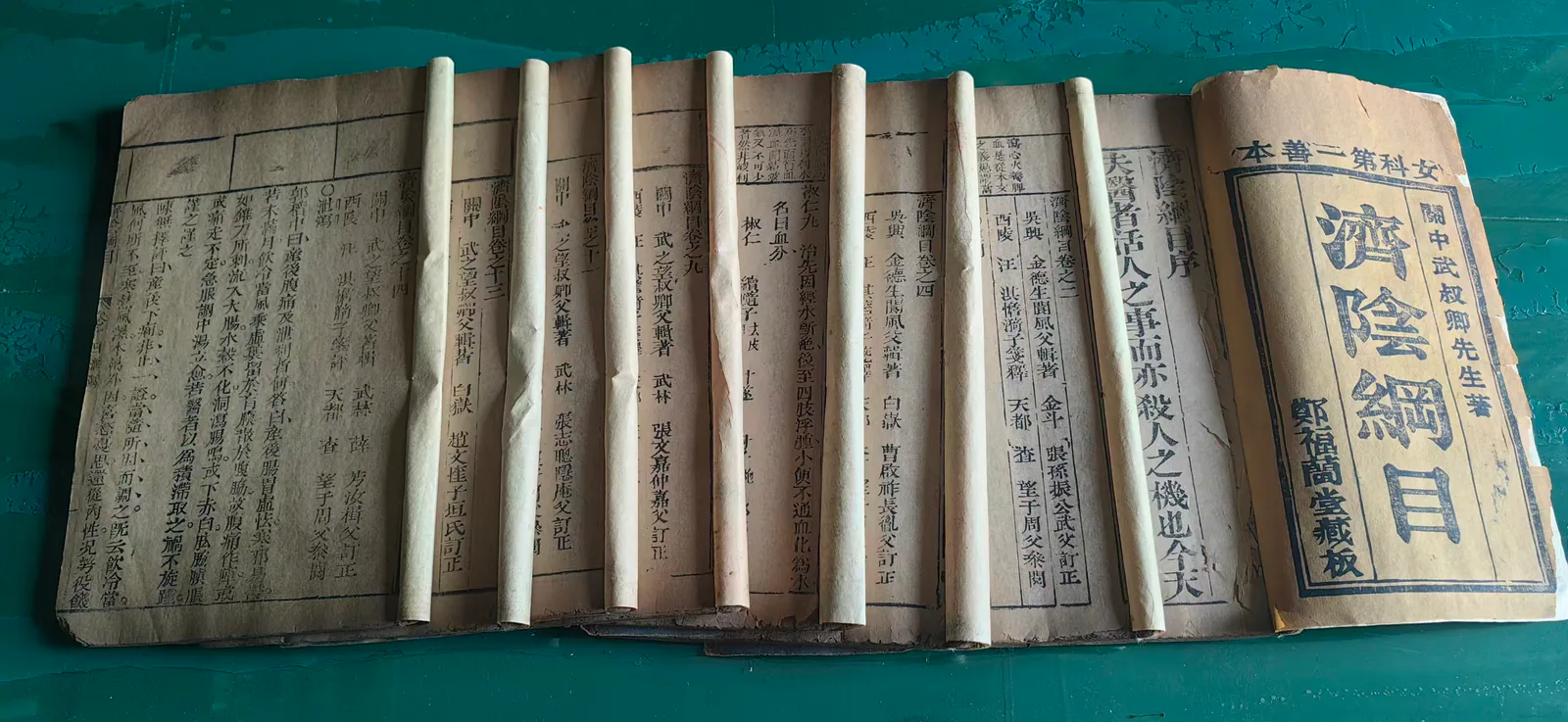 图片展示了郑福兰堂珍藏的《济阴纲目》多册线装本。书册封皮为橙黄，封面上有“郑福兰堂藏板”字样。书页内页为浅黄色，左侧有黑色繁体字的正文，右侧有白色繁体字的注释。书页间夹有白色纸条，部分纸条上有黑色文字。该图片与上下文紧密相关，直观呈现了郑福兰堂所藏的这部女科典籍，体现了其对妇科疾病的关注与专业诊疗态度。