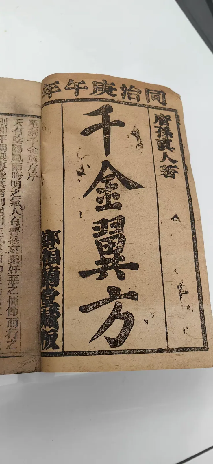 这张图片展示的是郑福兰堂珍藏的同治庚午年（1870年）刻印的古籍《千金翼方》，该书是孙思邈所著，书页泛黄，有着岁月留下的陈旧痕迹。书页顶部印有“同治庚午年”字样，右侧标注“唐孙真人著”，中间是醒目的书名“千金翼方”，左侧则有“郑福兰堂藏版”的字样，整体呈现出古医籍的厚重质感，和文档中提及的、承载着“大医精诚”医道的这部典籍相契合，是药堂百年传承的医德与医道的直观载体。