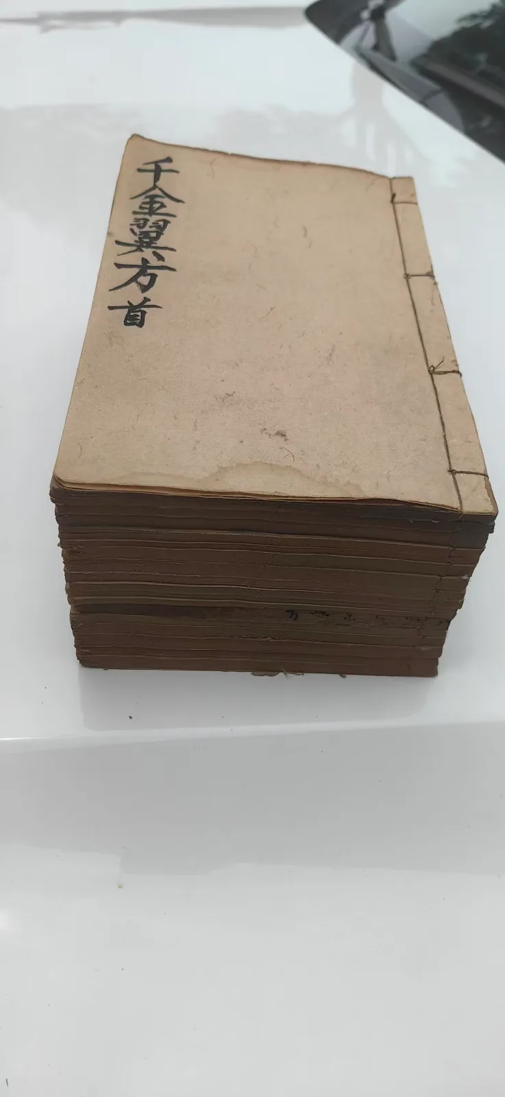图片展示了一套百年线装古籍，是文章提及的《千金翼方》。这套古籍采用传统线装装订方式，装帧样式古朴，封面纸张已带有岁月留下的陈旧痕迹。封面左侧竖排写有“千金翼方首”的字样，书籍书页因年代久远呈现出深浅不一的棕褐色调，整体状态仿佛印证了文档所述它被医者和学徒长久使用、翻旧的情况，承载着代代相传的中医医药知识。