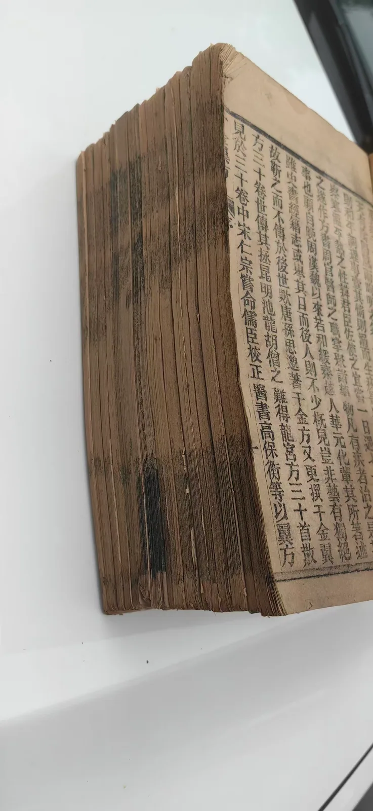 图片展示了一本古旧的医书，书页泛黄，部分书页有明显折痕和污渍，书脊处有黑色污渍。书页上密密麻麻地印有黑色小字，右侧有竖排文字。该书可能为《千金翼方》，因其被医者长期使用，经得起一代又一代人的检验，体现了其在医学界的重要地位。图片与上下文紧密相关，直观呈现了被翻旧了百年的《千金翼方》的样子，呼应了上文对这本医书经得起时间考验的描述。