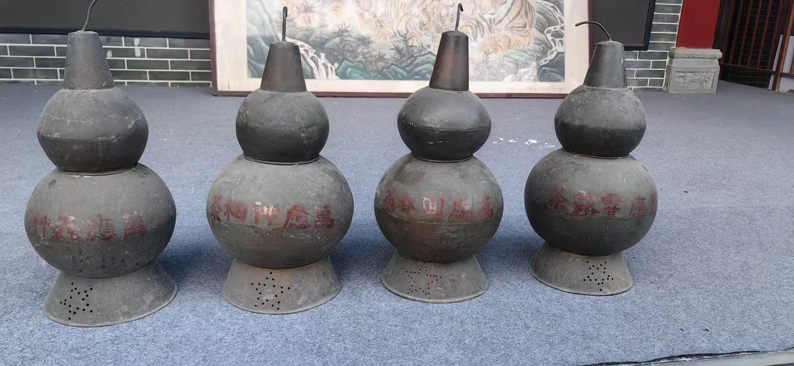 图片展示了郑福兰堂的四只凉茶壶。它们呈葫芦形，壶身由上下两部分组成，上部较细，下部较粗，整体呈圆润的葫芦状。壶身表面有“郑福兰堂”字样，底部有小孔。这些凉茶壶比普通茶壶高出一截，壶嘴短，壶盖尖，壶身上写有“万应甘露茶”“万应回春茶”字样，是郑福兰堂当年卖凉茶用的器具。