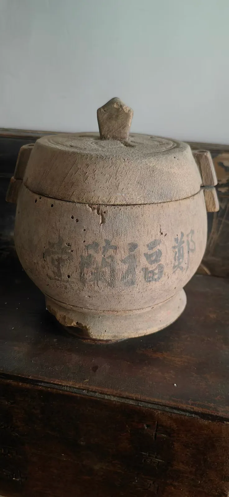 图片展示的是郑福兰堂的木质药材容器。容器呈圆柱形，盖子上有小孔，盖子和容器主体之间有木制把手。容器表面有“郑福兰堂”字样，盖子上还刻有“龙涎香”字样。该容器放置在木质桌面上，背景为浅色墙面。图片与上下文紧密相关，直观呈现了文中提到的“龙涎香名贵，也是一味药，老药号大约是专门用它来收存这一味料的——单放一罐，不混不串，才稳妥”的内容，展示了单放一味药材的“专放”容器。