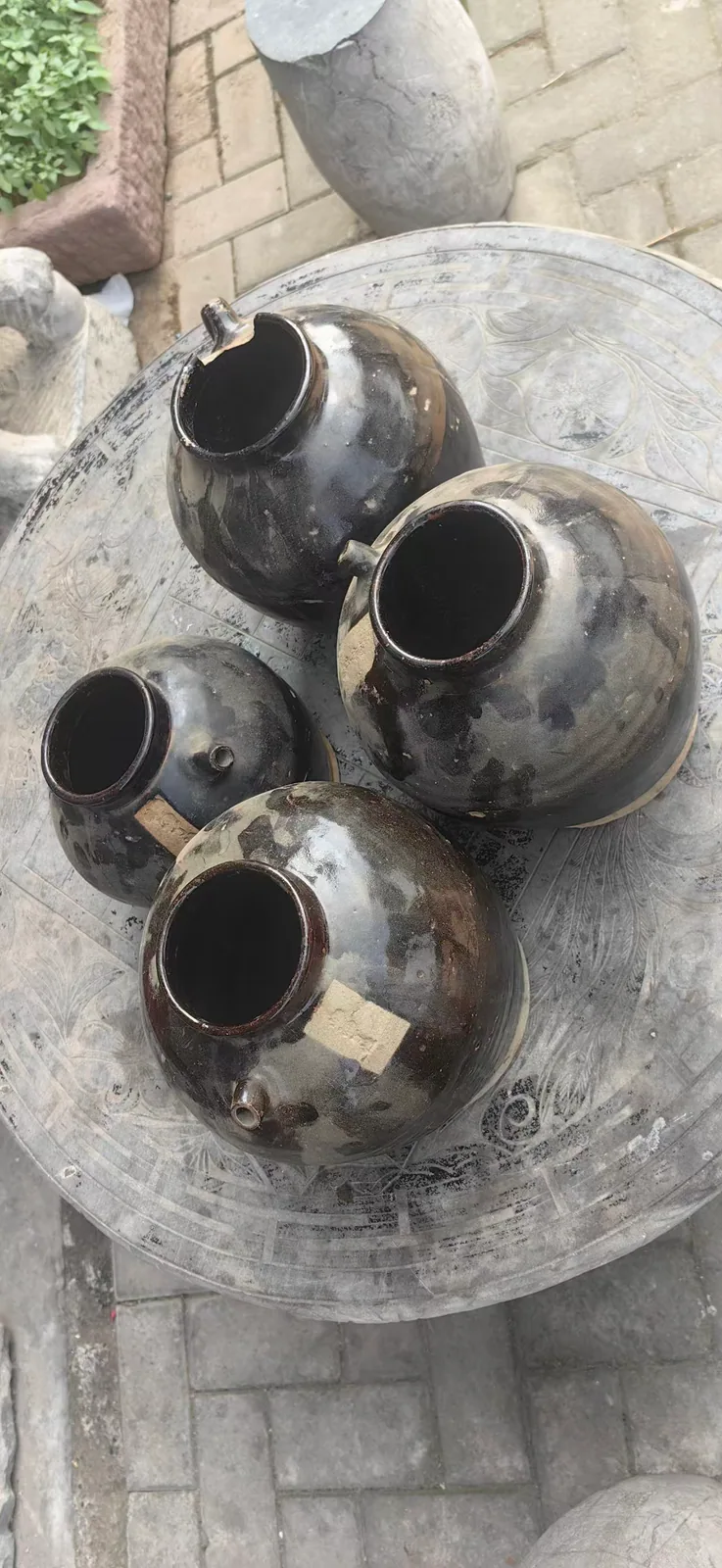 图片展示了郑福兰堂药酒泡制所用的陶坛。坛子呈深褐色，表面有自然的斑驳纹理，大小不一，排列在一张圆形石桌上。这些陶坛是药酒泡制的容器，需耐得住时间消磨，与上下文介绍的药酒需泡制数月甚至数年相呼应，体现了中医对器物日常讲究的传承。