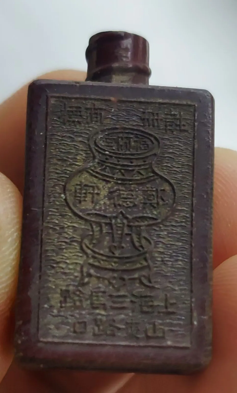 图片展示的是郑福兰堂的“八宝拨云散”眼药瓶。它比打火机还矮，深色，扁方形，瓶身正面刻有药名，背面刻有一只药壶图样。瓶口细小，便于控制眼药用量。古人穿衣讲究，可将其装在衣襟、袖袋等暗袋、荷包、腰带夹层中。因眼科用药急，眼睛不舒服时需随身携带，此瓶设计正符合这一需求。