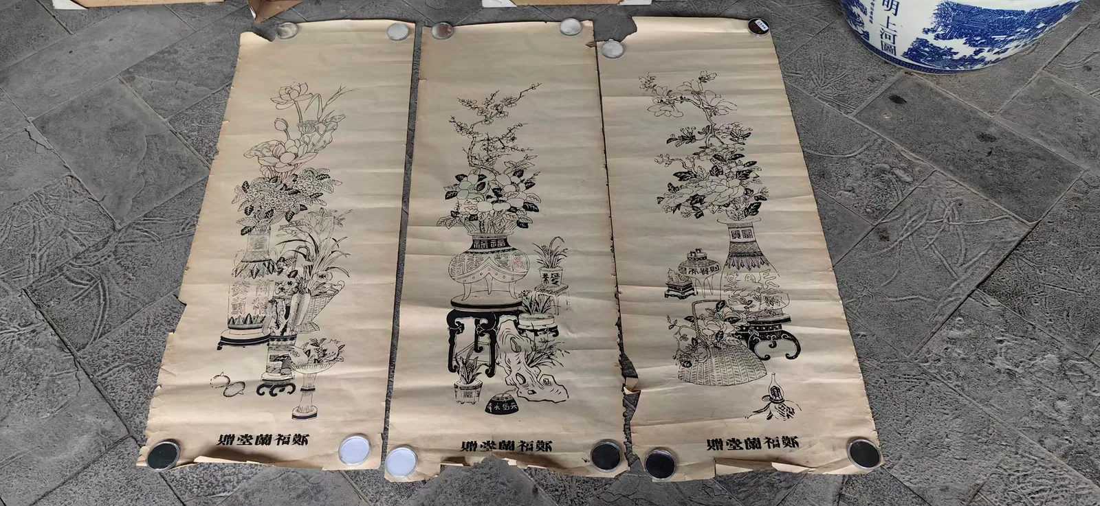 这张图片展示的是郑福兰堂用来赠送给顾客的平安富贵条屏，共三幅呈纵向并排摆放的条屏。每幅条屏均以线描方式绘制，画面核心是插有花束的花瓶、案几、盆栽等传统吉祥器物，底部标注有“鄭福蘭堂”的字样，整体色调素雅古朴，契合老药号赠送祝福的特质。这些条屏会被主人家挂在堂屋正中，成为能日日望见的药号印记，承载着郑福兰堂对顾客的祝福，也代表着老药号和街坊邻里间的牵挂。